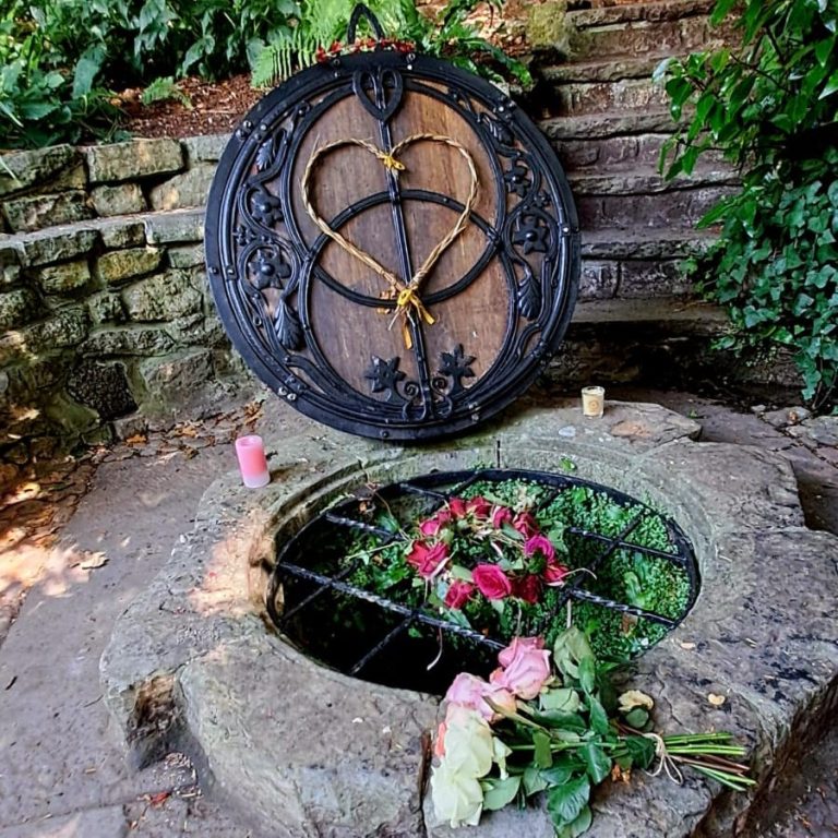 Limpieza energética hogar conciencia de corazon Placa decorativa sobre un pozo con flores y velas alrededor en un entorno natural.