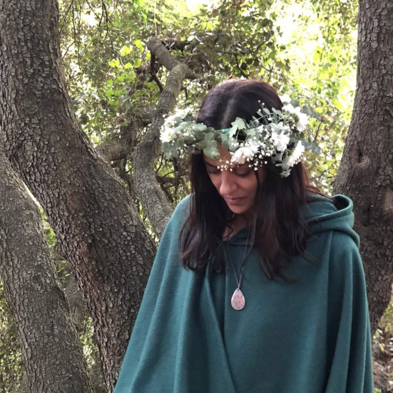 Limpieza energética conciencia de corazon Mujer con capa verde y corona de flores, mirando hacia abajo en un entorno natural.